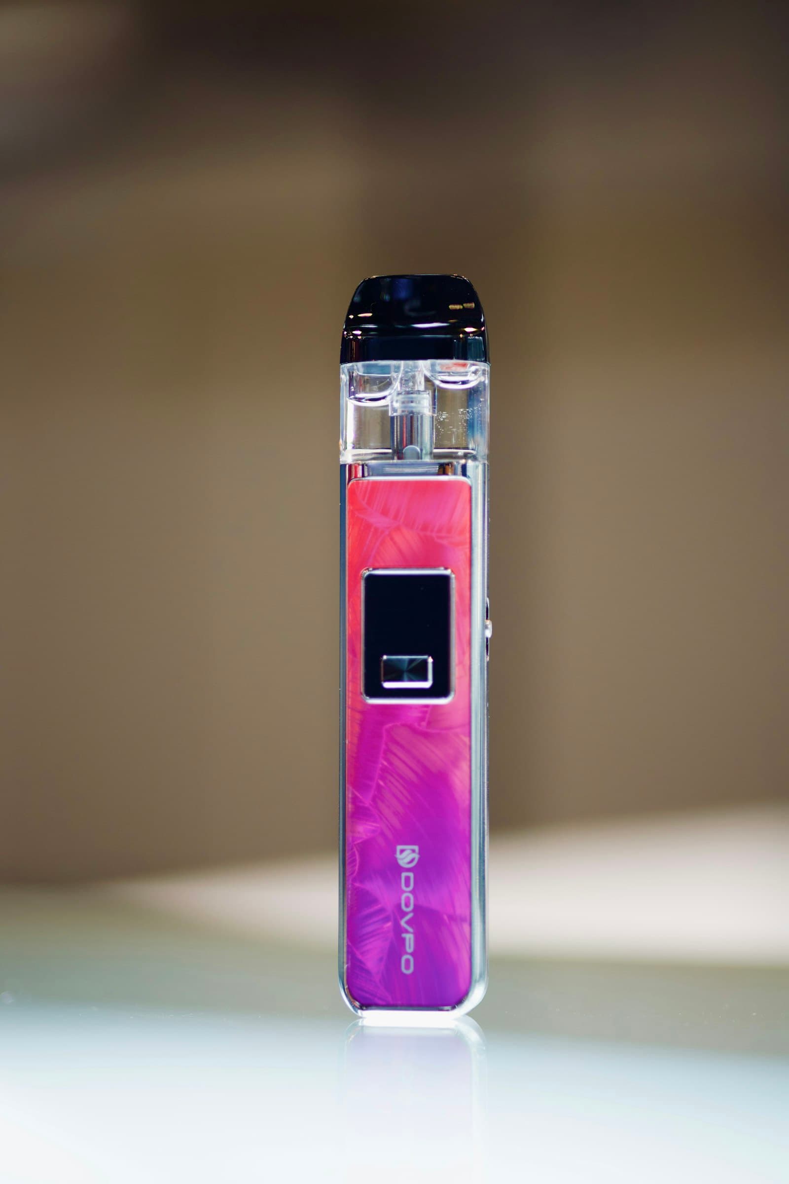 A rechargeable pod vape kit with a small display, standing upright on a light surface