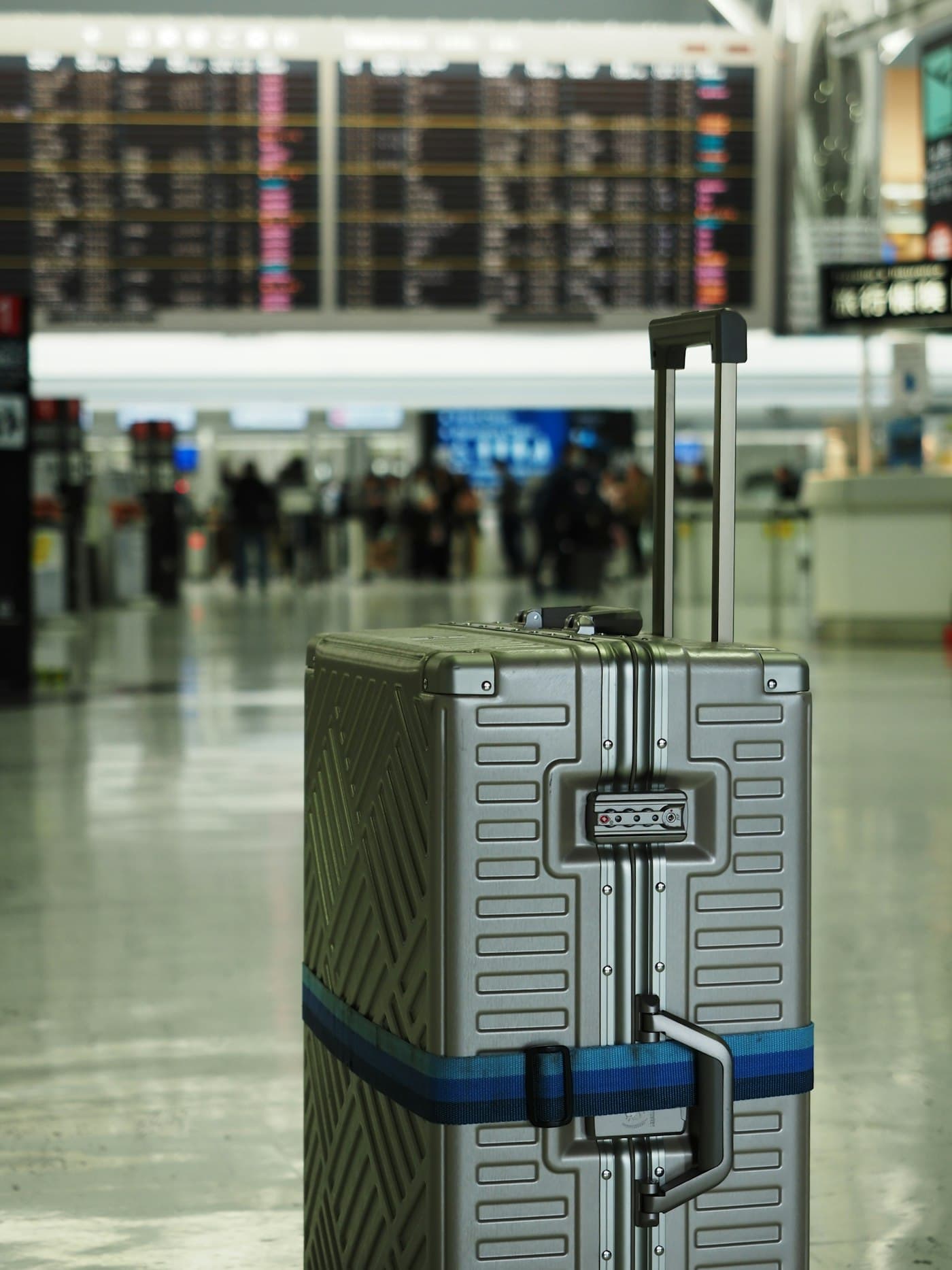 Hard-shell suitcase in an airport terminal with departure boards in the background