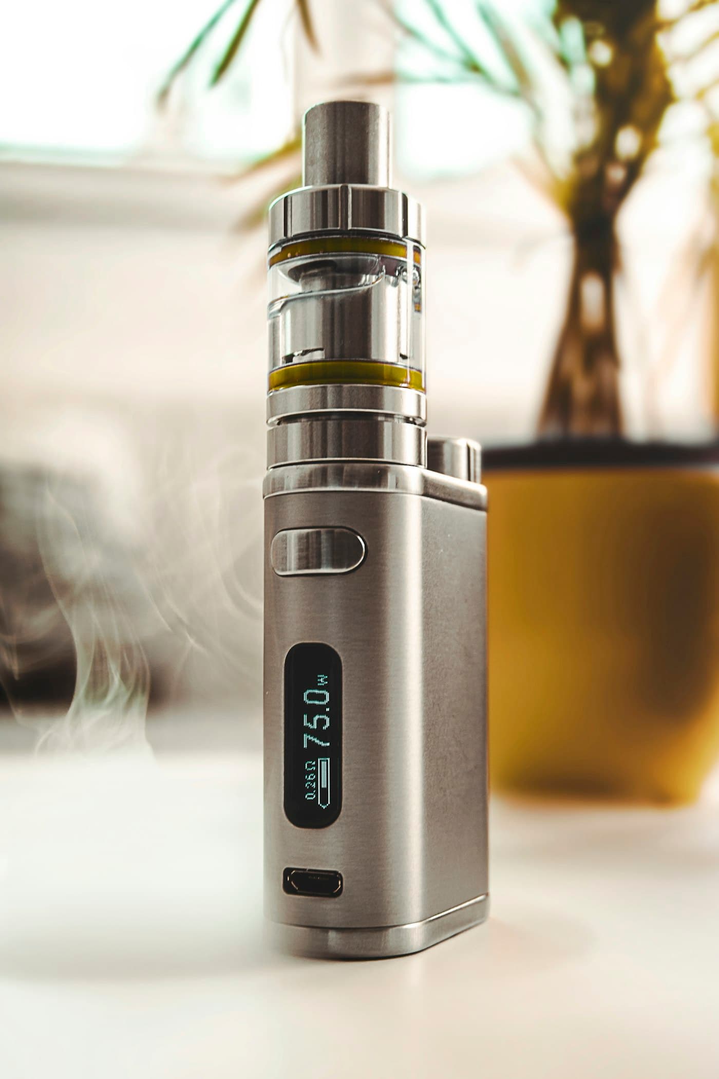 Grey pod vape device held upright showing its refill and coil compartment